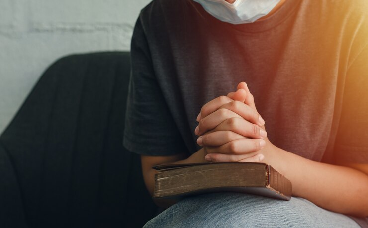 Foto oração de deus pedindo uma crise cristã uma jovem usando uma máscara ora a deus por uma vida melhor. mão feminina orando a deus com a bíblia peça perdão e fé na bondade