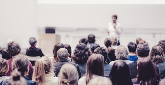 Orador feminino dando apresentação na sala de aula na oficina universitária Audiência na sala de conferências Vista traseira do participante não reconhecido na audiência Evento de conferência científica