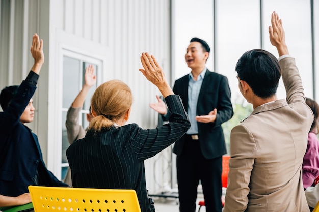 Un orador masculino dirige un seminario compartiendo experiencia con la audiencia diversa Los participantes levantan activamente sus manos haciendo preguntas y fomentando la cooperación y el aprendizaje