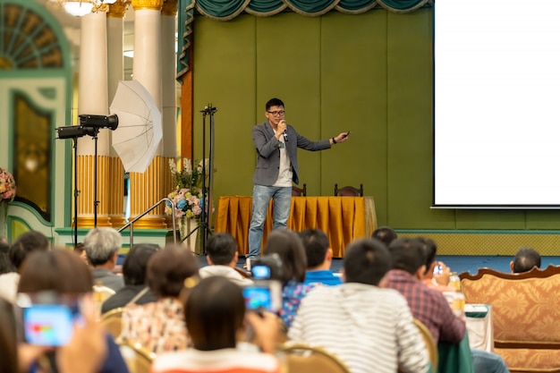 Oradora asiática con traje casual en el escenario presenta la pantalla en la sala de conferencias