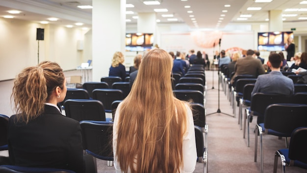 Oradora feminina dando apresentação na sala de aula na oficina universitária Vista traseira de participantes não reconhecidos ouvindo palestra e fazendo anotações Evento de conferência científica