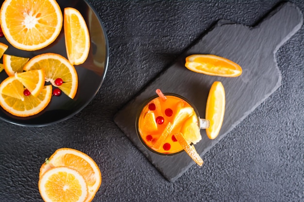 Orange Cranberry Fizzy Cocktail in einem Glas und Früchten daneben auf dunklem Hintergrund Hausgemachter Mocktail Draufsicht