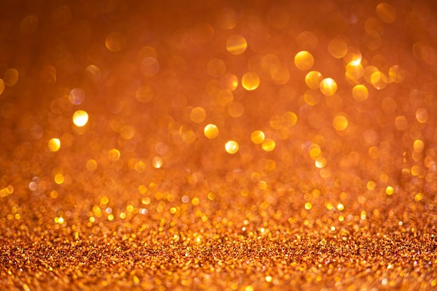 Orange glänzende Glitzertextur. Selektiver Fokus. Leuchtende Oberfläche, funkelnde Lichter und Bokeh-Effekte. Weihnachten und festliches Hintergrundfoto