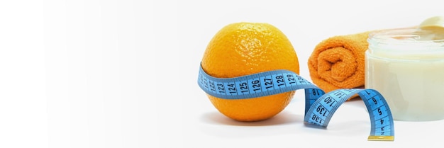 Orange ist mit blauem Maßband Körperpeeling und Handtuch auf weißem Hintergrund umwickelt