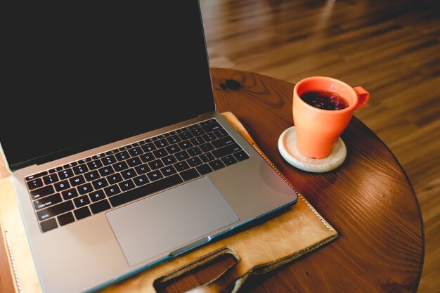 Orange Kaffeetasse und Laptop auf dem Tisch im Café.