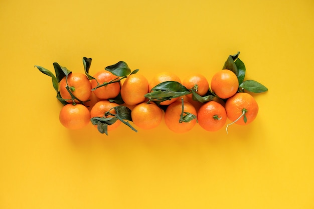 Orange Mandarine mit Blättern auf einer gelben Oberfläche