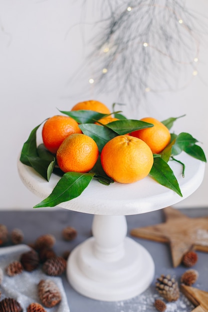 Orange Mandarinen auf grauem Hintergrund im Dekor des neuen Jahres mit braunen Tannenzapfen und grünen Blättern. Weihnachtsdekoration mit Mandarinen. Köstliche süße Clementine.