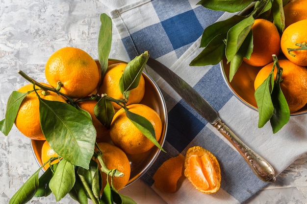 Orange reife Mandarine trägt mit grünen Blättern in den Schüsseln, über rustikalem weißem hölzernem Hintergrund Früchte.