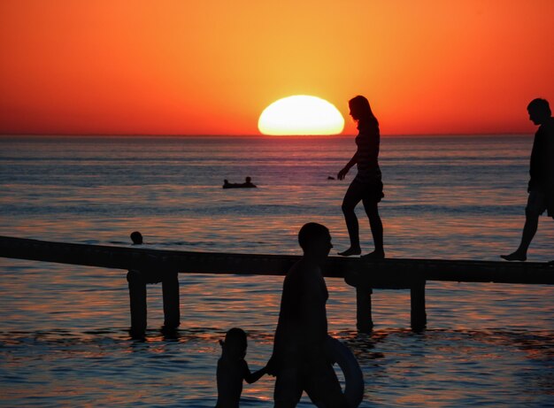 Foto orange sonnenuntergang auf dem meer mit silhouetten von urlaubern auf dem pier.