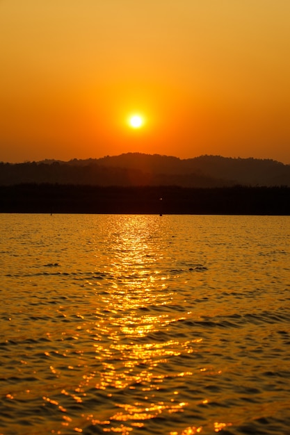 Orange Sun hasta la puesta de sol sobre la montaña y se refleja en el río con la sombra del árbol lejano.