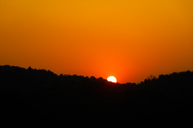 Orange Sun hasta la puesta de sol sobre la montaña y se refleja en el río con la sombra del árbol lejano.