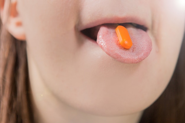 Orange Tablette auf der Zunge eines Mädchens