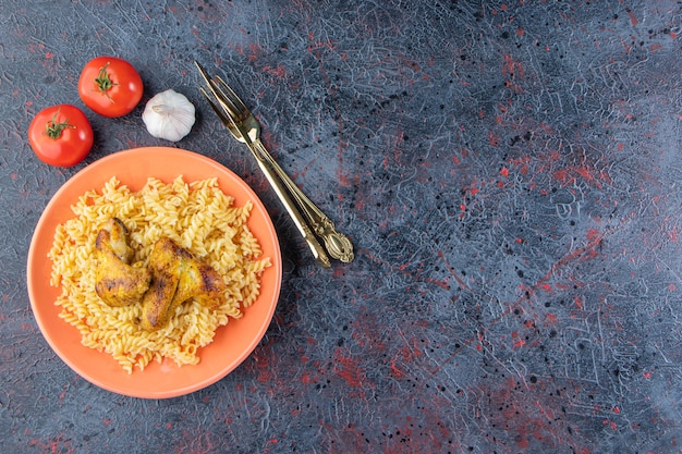 Orange Teller mit Fusilli-Nudeln mit gebratenen Hühnerflügeln auf Marmoroberfläche.