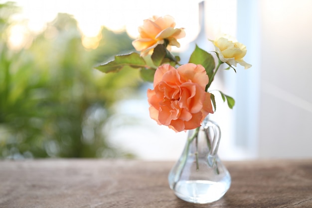 Orange und gelbe Rosen in transparenter Vase auf braunem Holztisch