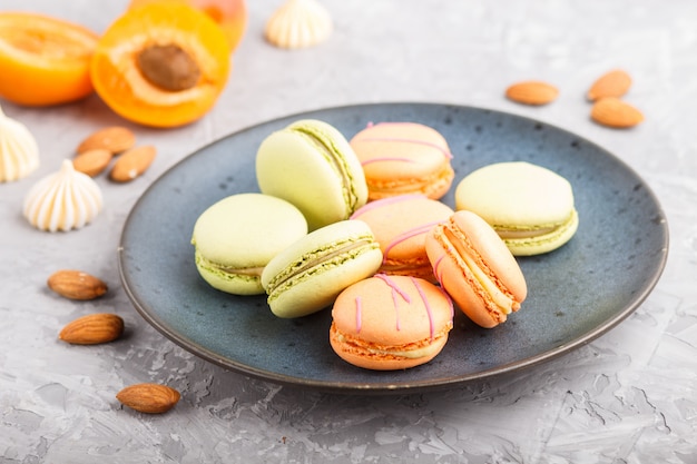 Orange und grüne Macarons oder Macaroons-Kuchen auf blauer Keramikplatte auf einer grauen Betonoberfläche. Seitenansicht, selektiver Fokus.