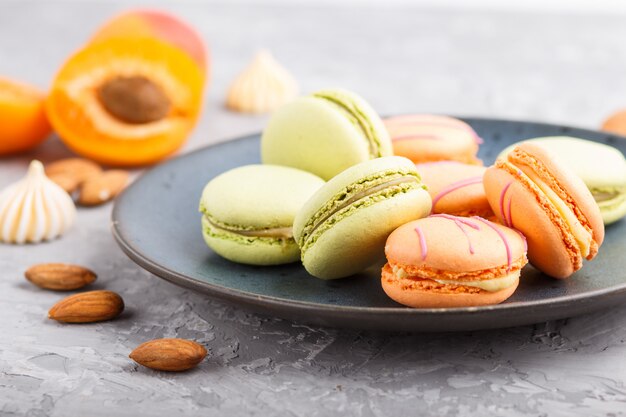 Orange und grüne macarons oder Makronen backt auf blauer keramischer Platte auf einem grauen konkreten Hintergrund zusammen. Seitenansicht, selektiver Fokus.