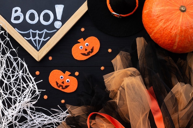 Orange und schwarzes Halloween-Flatlay. Kreideaufschrift BOO, Kürbisse aus Filz, Tüll, Spinnennetz auf schwarzem Hintergrund.