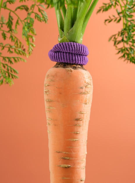 Orangefarbene Karotte mit dicken grünen Blättern und violettem Sport-Stirnband. Idee gesunder Lebensstil und Sport.