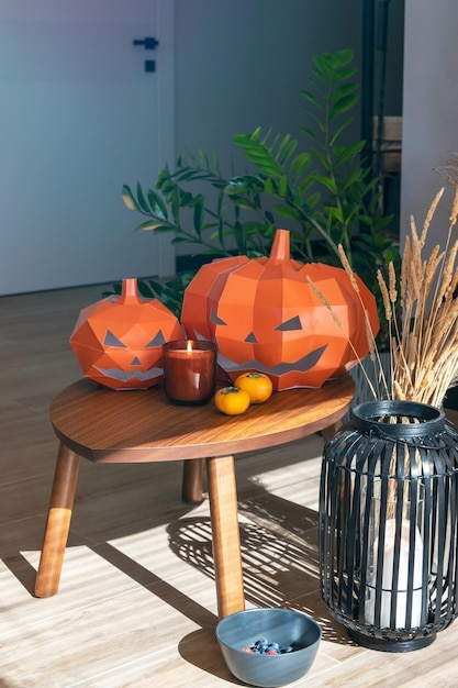 Orangefarbene Kürbisse aus Pappe für Halloween. Installation mit Kerzen und Obst auf dem Tisch