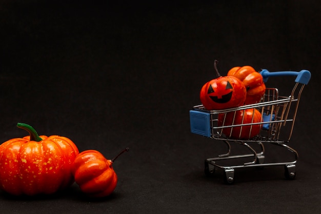 Orangefarbene Kürbisse in einem Wagen und verstreute Kürbisse auf schwarzem Hintergrund. flat lei zum thema verkauf in halloween. Platz kopieren