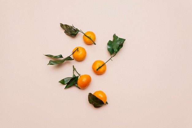 Orangefarbene Mandarinen mit grünen Blättern, die auf beigem Hintergrund verstreut sind Clementine Mandarine Draufsicht Flach lag