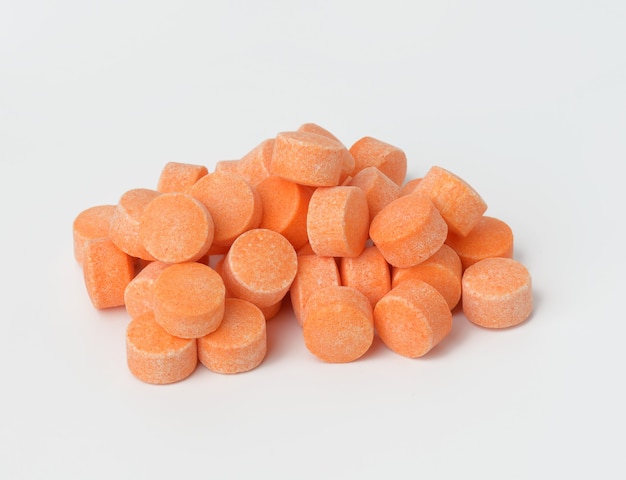 Orangefarbene Pillen auf weißer Oberfläche, Vitamin C, Nahaufnahme