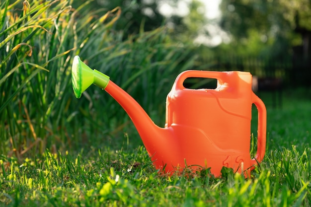 Orangefarbene Plastikgießkanne steht auf dem grünen Gras im Sommergarten