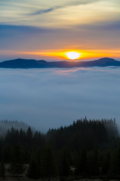 Orangefarbene Sonnenstrahlen am Morgen über nebligen Wolken in den Bergen