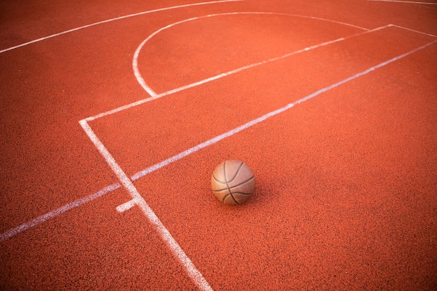 Orangefarbener Ball der Draufsicht für den Basketball, der auf dem Gummisportplatz liegt. Sport roter Boden im Freien