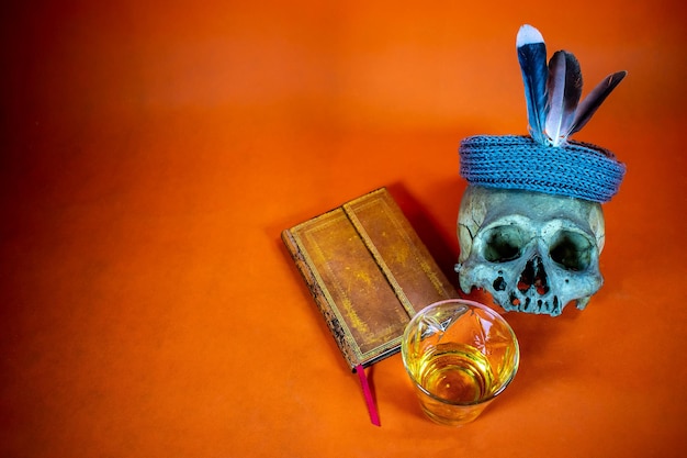 Orangefarbener Hintergrund mit alten Büchern, einem Schädel und einem Glas Alkohol. Platz zum Einfügen von Text