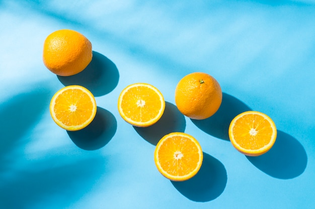 Orangen auf einer blauen Oberfläche unter natürlichem Licht mit Schatten. Hartes Licht. Konzept der Ernährung, gesunde Ernährung, Erholung in den Tropen, Urlaub und Reisen, Vitamine.