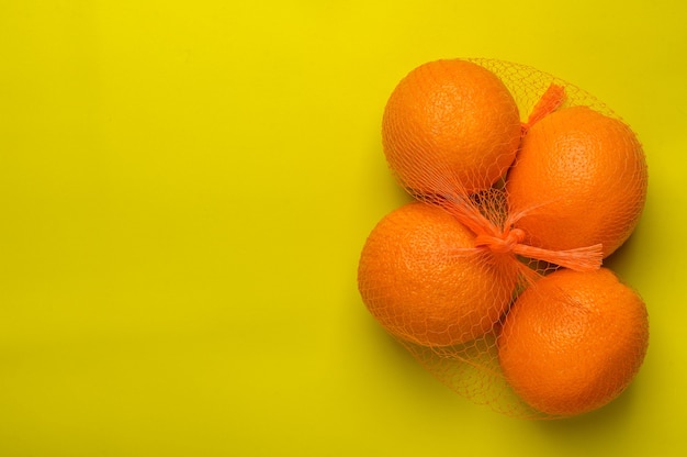Orangen in einem Gitter auf einer gelben Oberfläche Draufsicht