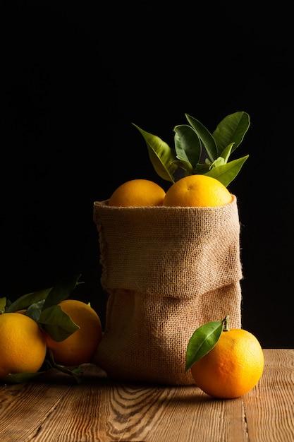 Orangen in einem Leinensack und auf einem Holztisch auf dunklem Hintergrund