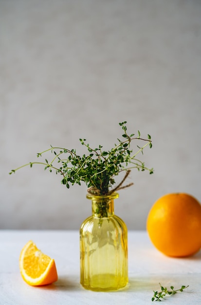 Orangen-Thymian oder Thymus Citriodorus-Bündel in gelber Vase mit geschnittenen Orangen