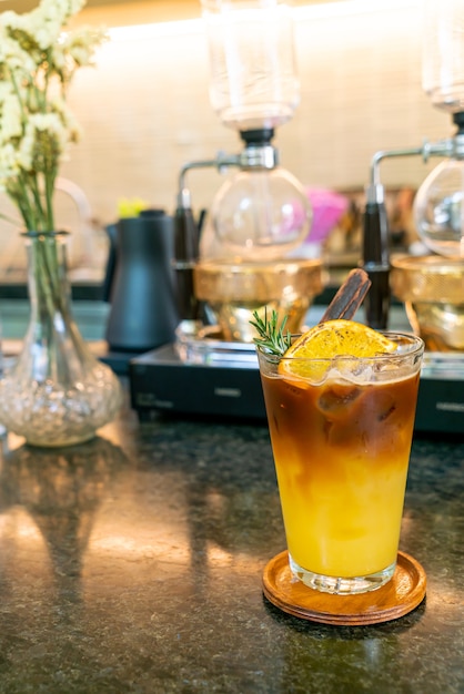 Orangen- und Zitronensaft-Soda mit schwarzem Kaffee in Glas mit Rosmarin und Zimt