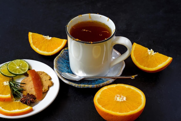 Orangen-Zimt-Tee mit kristallisierten Früchten und Keksen auf schwarzem Hintergrund