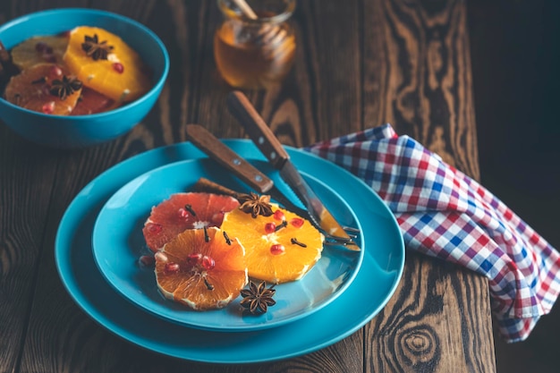 Orangendessert mit Weinhonig oder Ahornsirup und Ingwergewürz verzierte Granatapfelbeeren auf blauem Teller Wunderbar süßes, reichhaltiges und frisches Essen Dunkler rustikaler Hintergrund