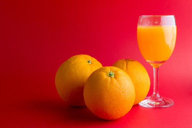 Orangenfrucht mit Orangensaft im Weinglas auf rotem Hintergrund