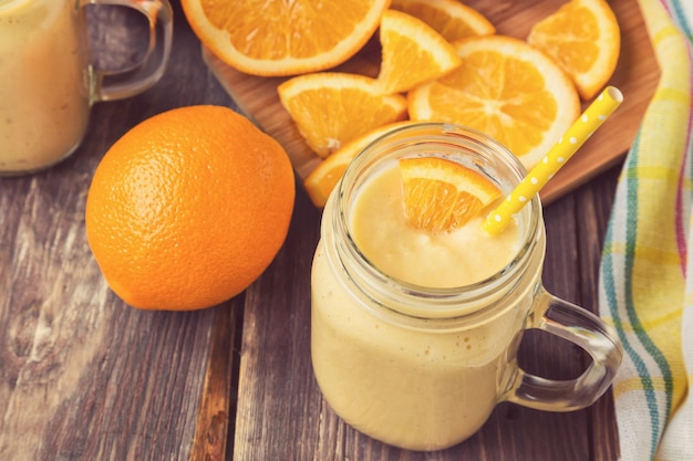 Orangenfrucht-Smoothie im Glas mit frischen Orangenscheiben auf rustikaler Holzoberfläche