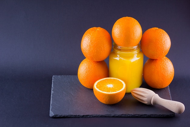 Orangenfrüchte und Saft. Zitrusfrüchte zur Saftherstellung mit Handentsafter. Orangen auf Schieferplatte. Einmachglas mit Orangensaft