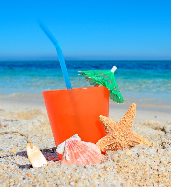 Orangengetränk mit Muschel und Regenschirm an einem tropischen Strand