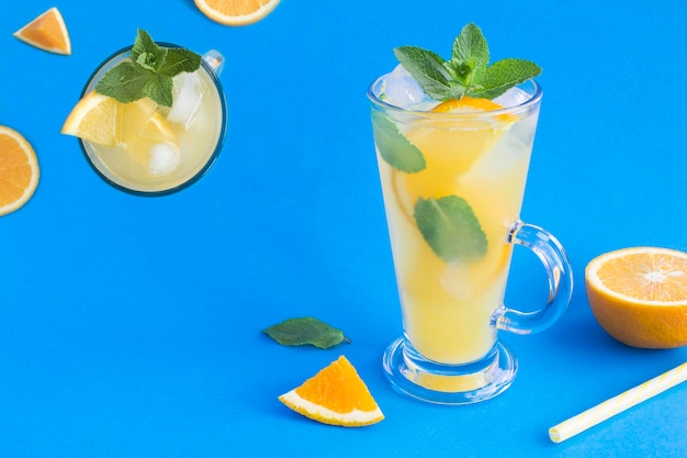 Orangengetränk oder Limonade mit Minze und Eis im Trinkglas auf blauem Hintergrund Nahaufnahme Kopierbereich