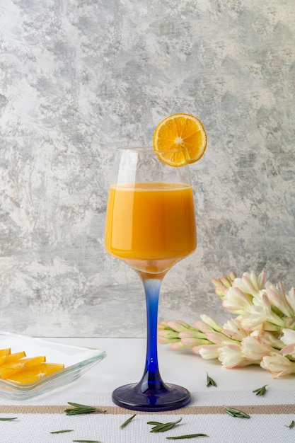 Orangengetränk serviert in einem Kristallglas mit einer Scheibe und einer Vase auf dem Tisch