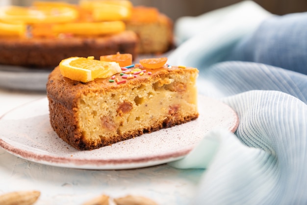 Orangenkuchen mit Mandeln und einer Tasse Kaffee auf weißem Betonhintergrund und blauem Leinentextil. Draufsicht, Nahaufnahme,