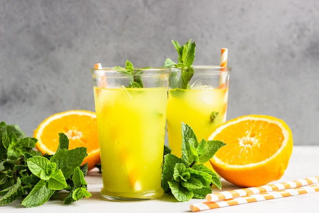 Orangenlimonade im Glas mit frischer Orange und Minze über hellgrauer Steintabelle. Erfrischendes Sommergetränk. Cocktailbar