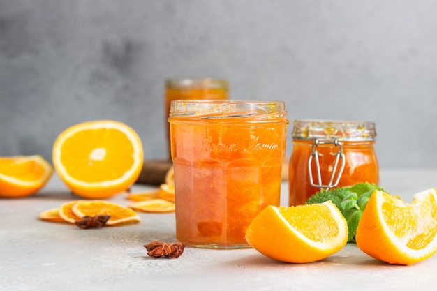 Orangenmarmelade im Glas, Orangenscheiben, Minze und Gewürzen auf hellgrau