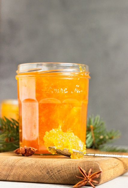 Orangenmarmelade in einem Glasgefäß mit Wintergewürzen und -tannenzweigen.