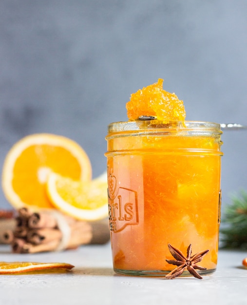 Orangenmarmelade in einem Glasgefäß mit Wintergewürzen und -tannenzweigen.