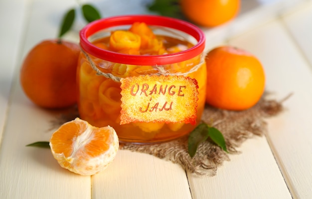 Orangenmarmelade mit Schale und Mandarinen, auf weißem Holztisch