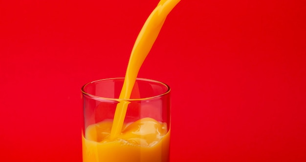 Orangensaft, der in das Glas, getrennt auf rotem Hintergrund gießt